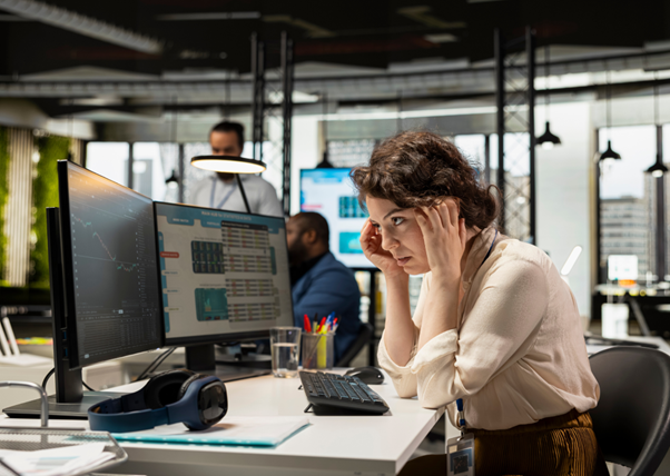 A founder sitting at her desk with her head in her hands, several monitors open in front of her — the kind of operational overwhelm that prompts small-business owners to consider outsourcing.